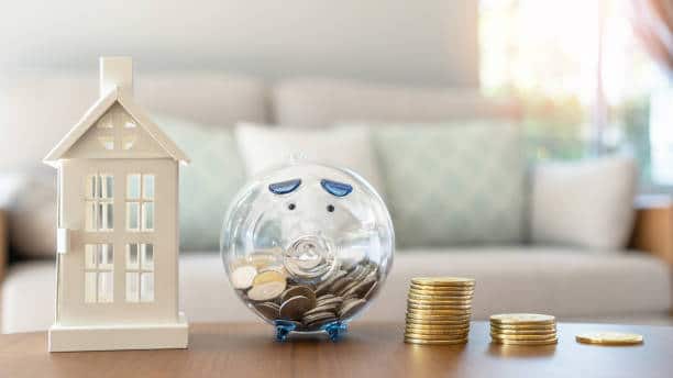 Maison en plastique posé à coté d'une tirelire cochon avec des pièces dedans pour symboliser les économies à la suite de la renégociation du taux de prêt d'un crédit immobilier